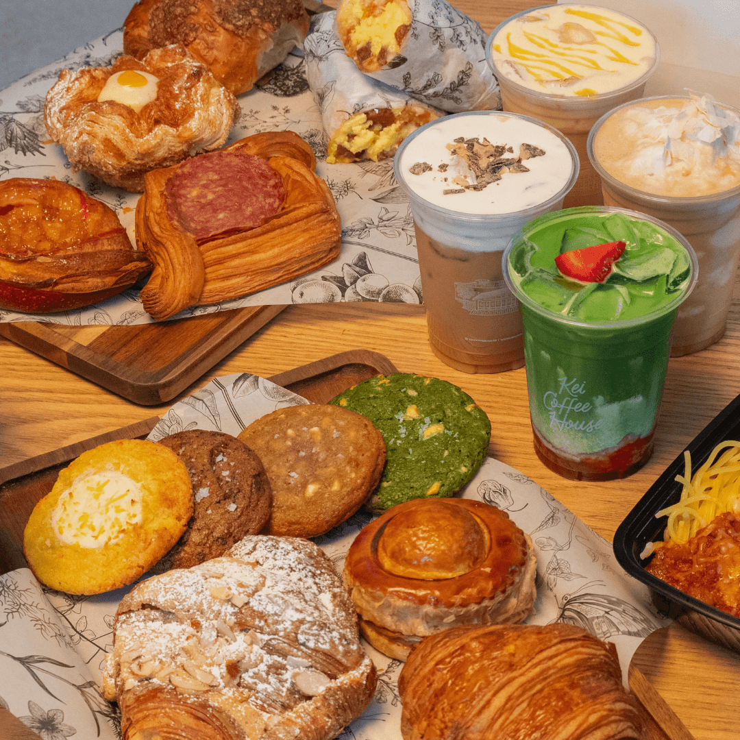 A spread from Kei Coffee House featuring assorted cookies, strawberry matcha, toffee latte, pastries including pâté chaud, and signature baked treats like the cheese corn cookie arranged on wooden trays and tables.