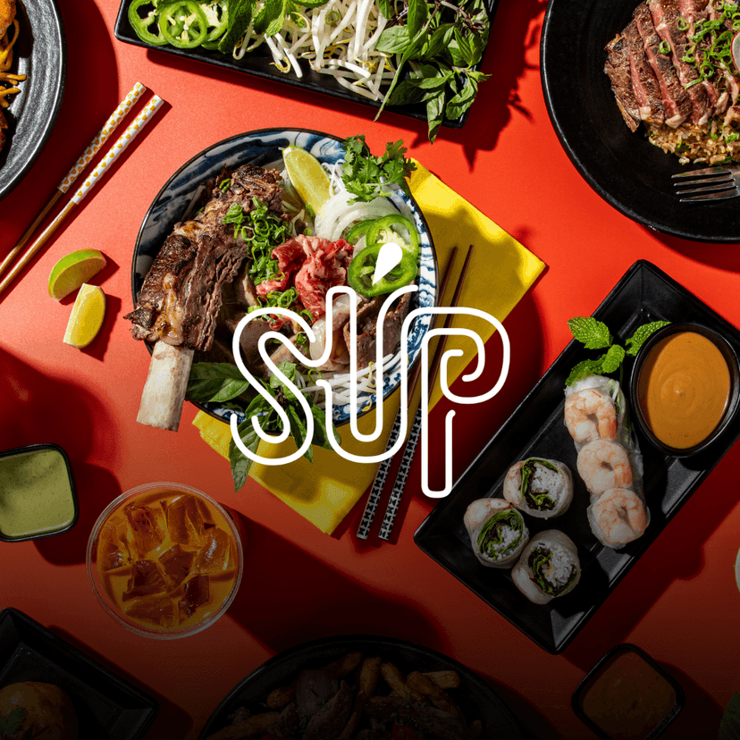 SUP Noodle Bar logo overlaid on a vibrant spread of the restaurant’s signature dishes, including combination pho, shrimp spring rolls with dipping sauce, fresh herbs, sauces, and Vietnamese-inspired plates arranged across a bright red table.